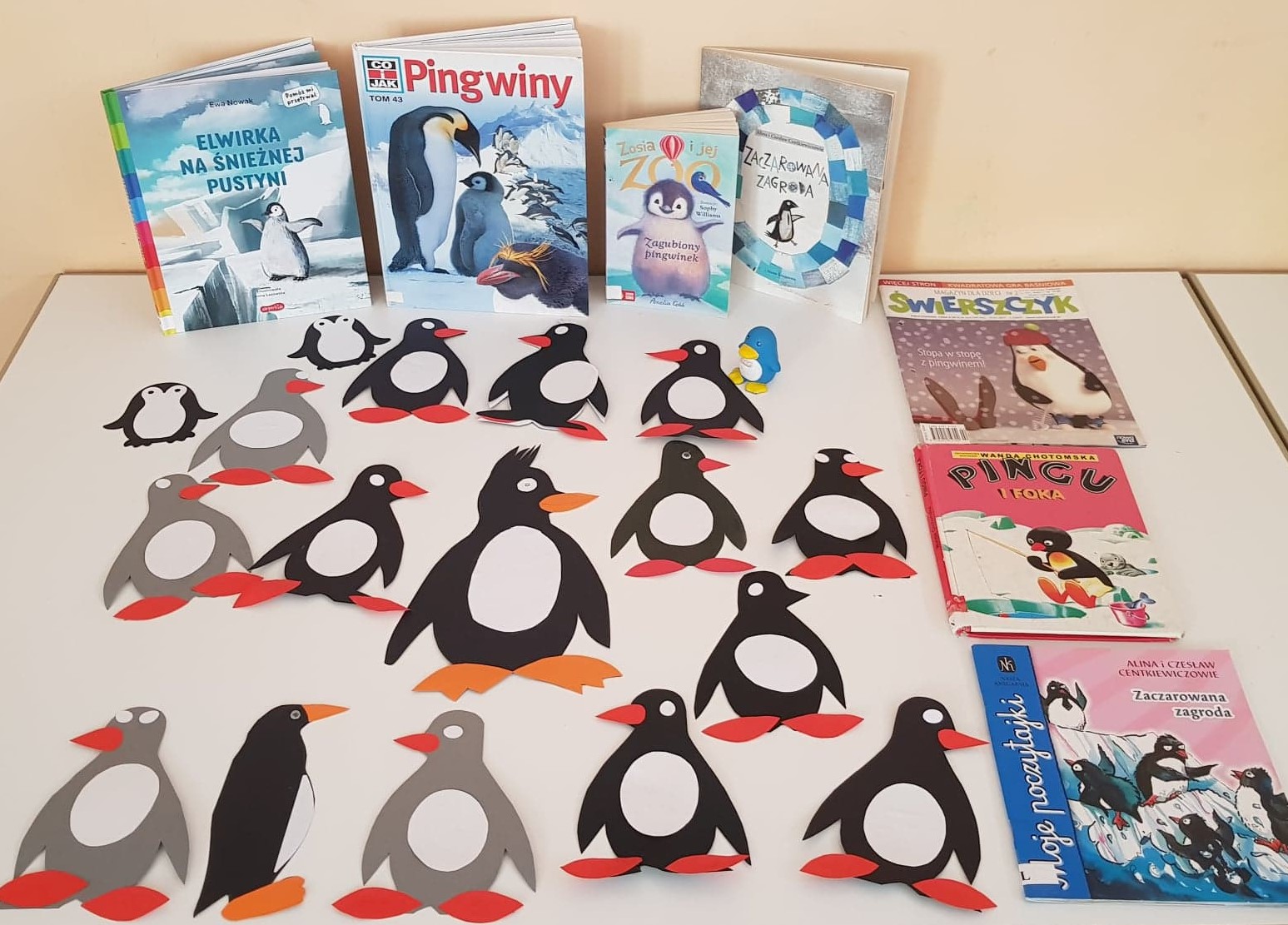 Na stole wyłożone są książki z ilustracją pingwinów na okładce orazPrace plastyczne przedstawiające pingwinki wykonane przez dzieci.