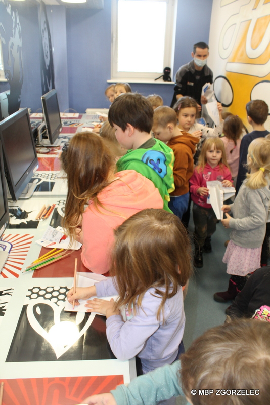 W pomieszczeniu biblioteki, grupa przedszkolaków koloruje samoloty z papieru