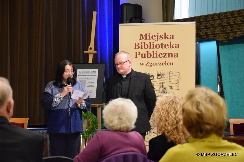 Spotkanie autorskie z ks. Adamem Szpotańskim w sali widowiskowej Miejskiego Domu Kultury w Zgorzelcu. Bibliotekarka zapowiada gościa spotkania - Adama Szpotańskiego. Zdjęcie jest jednocześnie odnośnikiem do artykułu "Pierwsza monografia Zgorzelca".