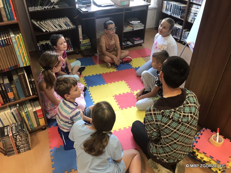 W pomieszczeniu biblioteki na piankowej macie siedzi 8 osób. Dzieci po kolei opowiadają z czym kojarzy im się słowo instrukcja.