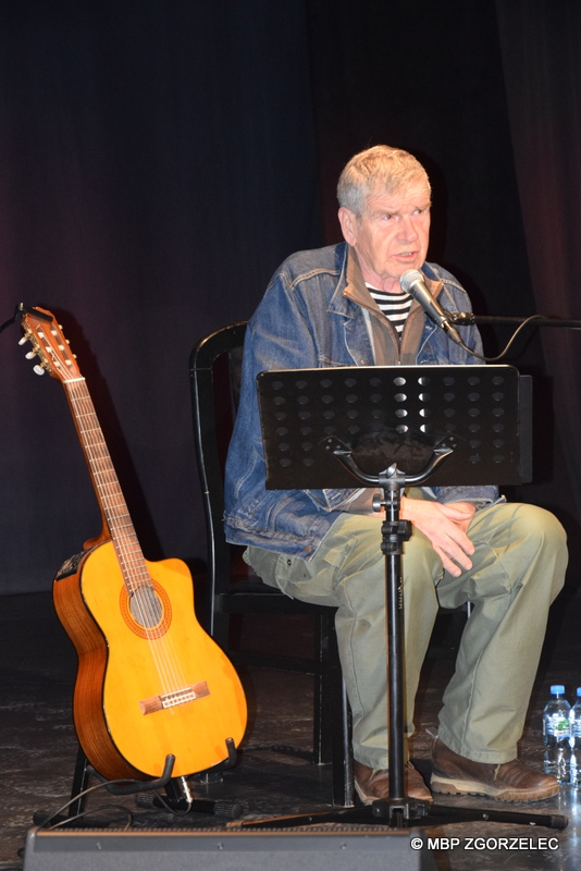 Lech Dyblik na spotkaniu w sali widowiskowej Miejskiego Domu Kultury w Zgorzelcu. Po lewej stronie aktora stoi gitara akustyczna.