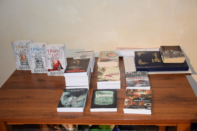 Kolekcja książek autorstwa Jolanty Marii Kalety, ułożona na drewnianym stole.