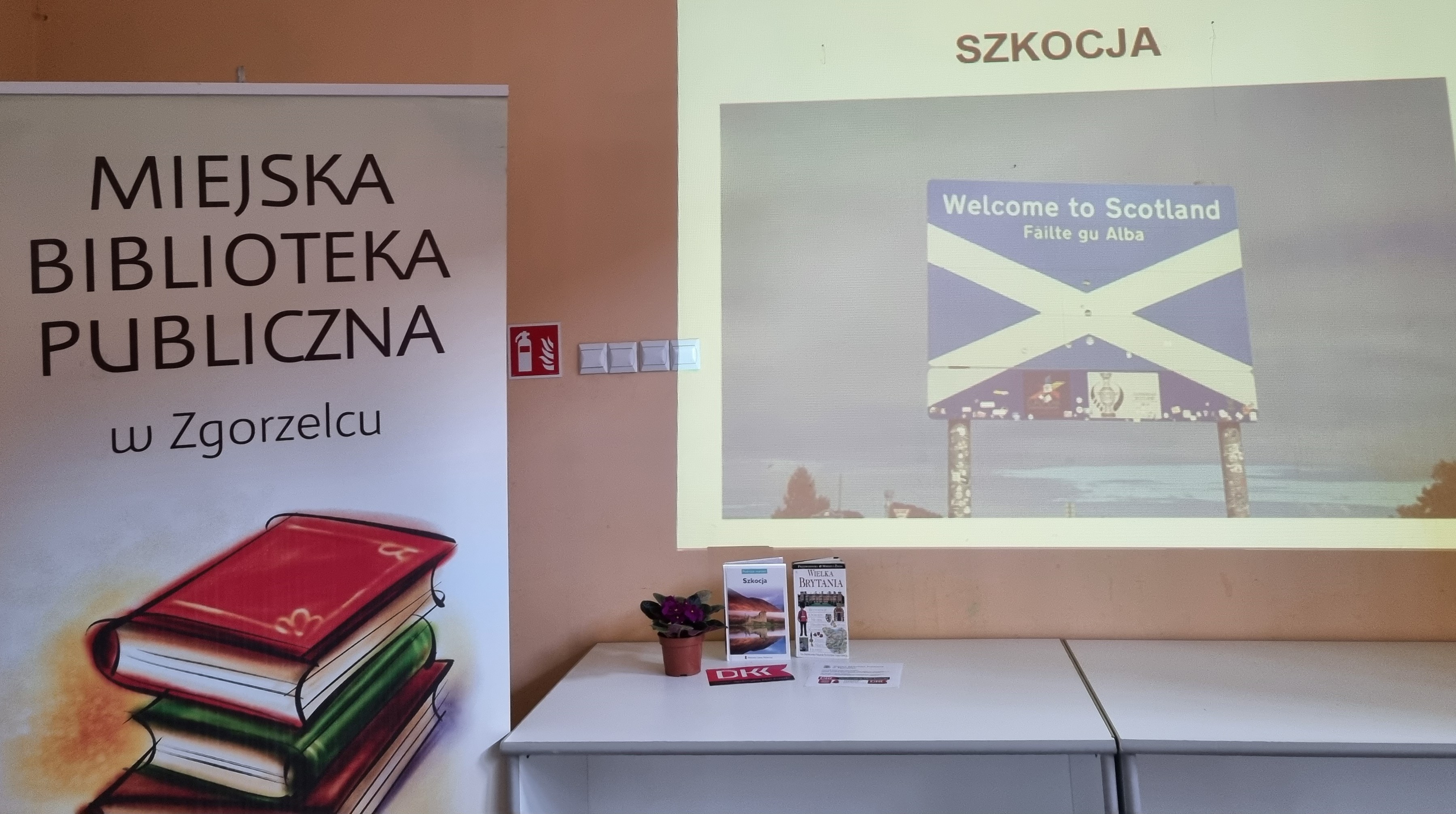 Na ścianie wyświetlony jest za pomocą projektora slajd z prezentacji dotyczącej Szkocji. Obok widać baner z napisem "Miejska Biblioteka Publiczna w Zgorzelcu"