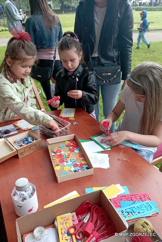 Przy stoliku trzy dziewczynki przygotowują laurki i zakładki okolicznościowe z okazji Dnia Matki