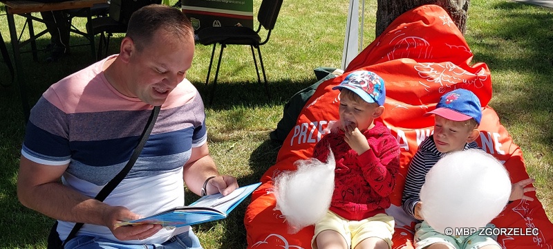 Na terenie otaczającym Fort Bolka i Lolka są trzy osoby, które siedzą na pufie. Mężczyzna czyta dzieciom książki.