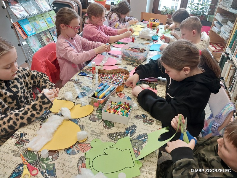 W pomieszczeniu Oddziału Dla Dzieci Miejskiej Biblioteki Publicznej w Zgorzelcu, grupa dzieci wykonuje prace plastyczne.