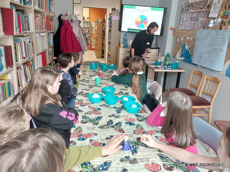 W pomieszczeniu biblioteki, grupa dzieci wykonuje prace plastyczne.