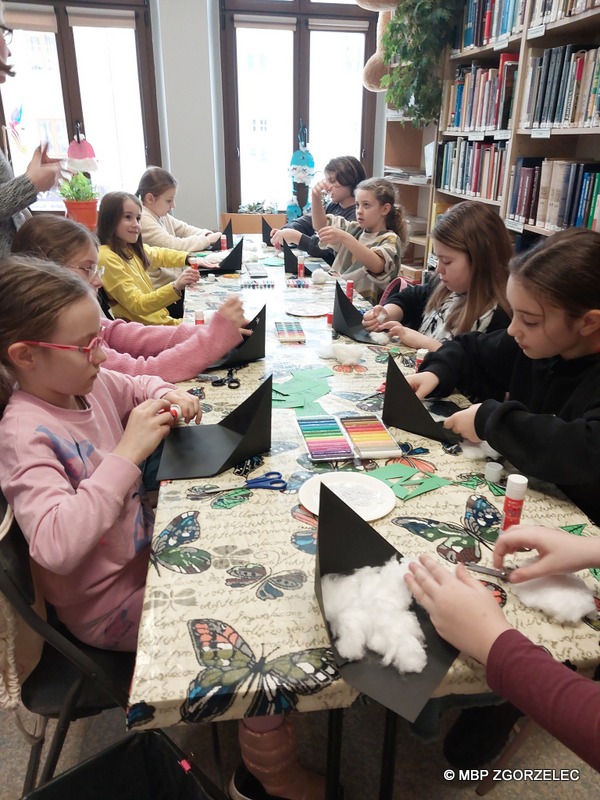W pomieszczeniu biblioteki, grupa dzieci wykonuje prace plastyczne.