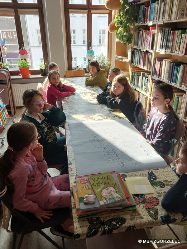 W pomieszczeniu biblioteki, grupa dzieci wykonuje prace plastyczne.