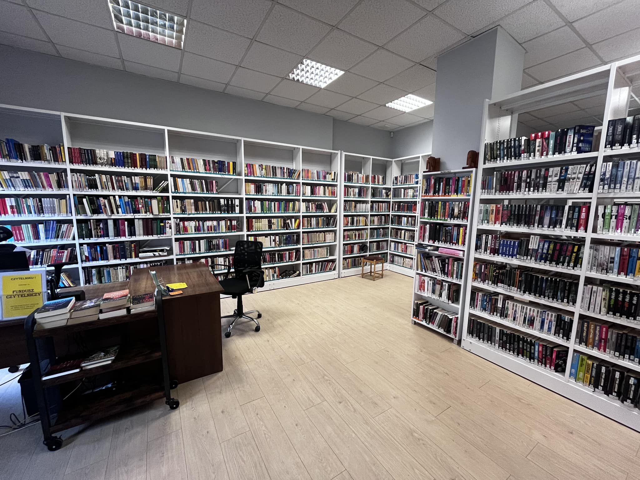 Nowocześnie urządzone pomieszczenie biblioteczne, ze stanowiskiem obsługi i regałami pełnymi książek