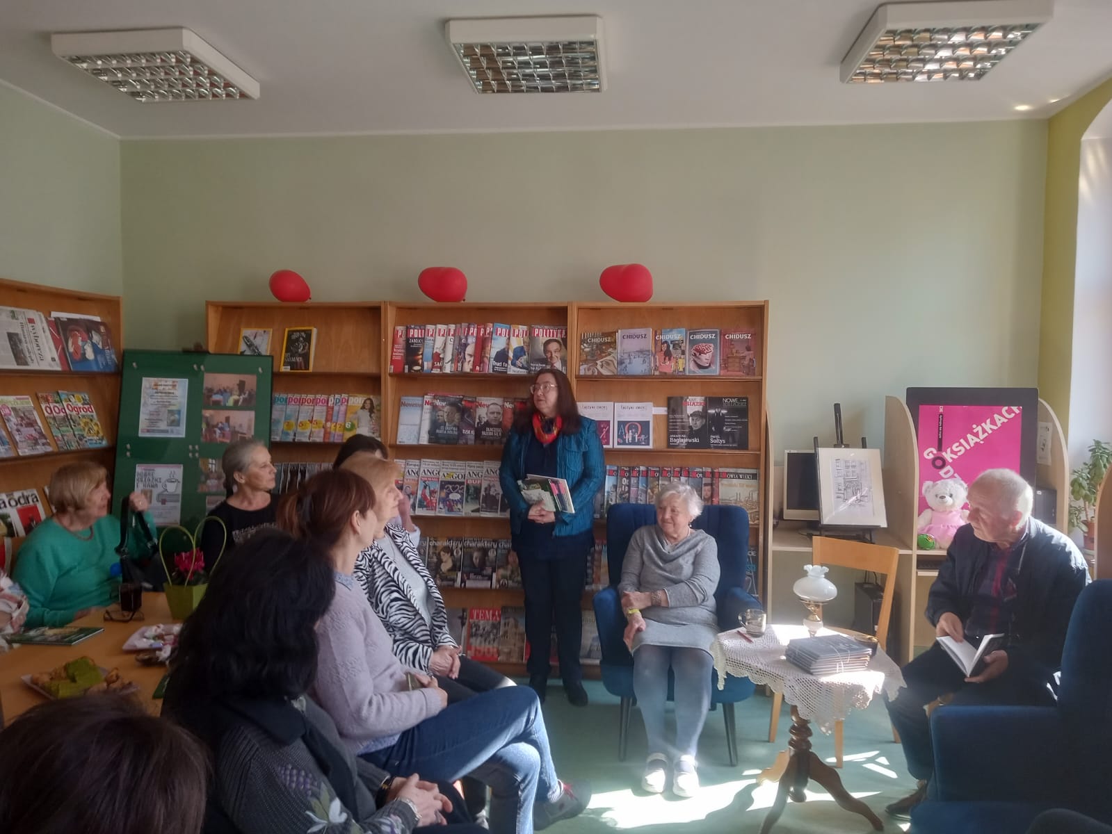 Autorka siedzi w czytelni biblioteki podczas spotkania z grupą czytelników.