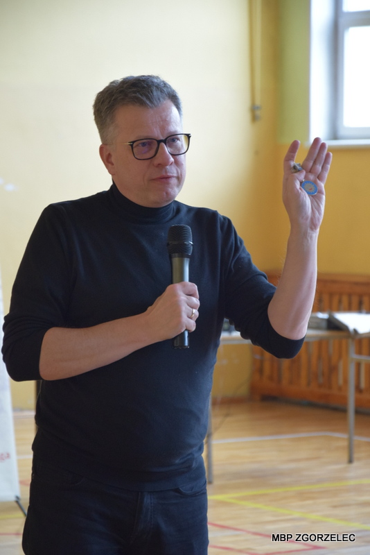 W pomieszczeniu sali gimnastycznej Szkoły Podstawowej nr 5 im. Marii Skłodowskiej-Curie, pan Marek Michalak pokazuje dzieciom Order Uśmiechu.