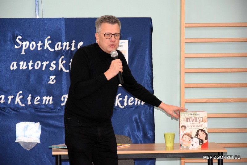 W pomieszczeniu sali gimnastycznej Szkoły Podstawowej nr 2 z Oddziałami Integracyjnymi im. Jarosława Iwaszkiewicza, pan Marek Michalak opowiada dzieciom o swoich książkach.