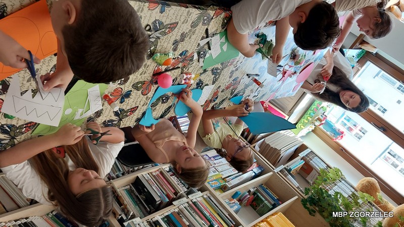 Dzieci wycinają i tworzą prace plastyczne przy stole w bibliotece.