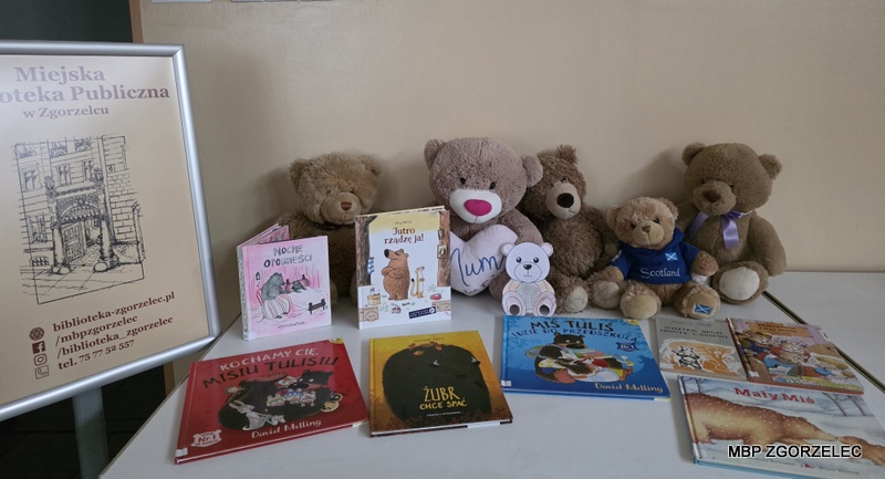 Na stole stoją pluszowe misie i książki o tematyce związanej z misiami, obok plakat z informacjami Miejskiej Biblioteki Publicznej w Zgorzelcu.