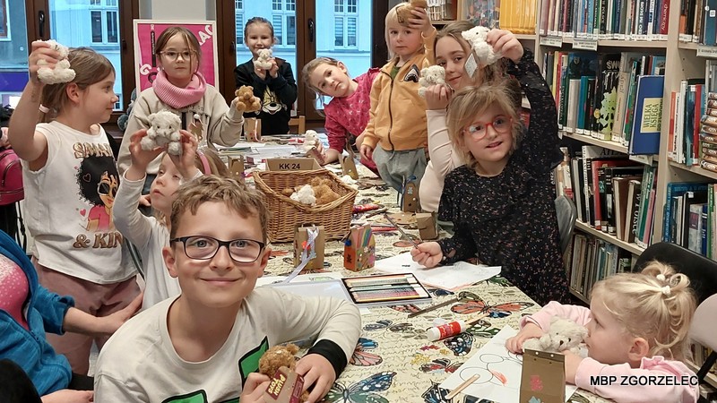 Dzieci prezentują swoje maskotki – grupa dzieci przy stole trzyma pluszowe misie.