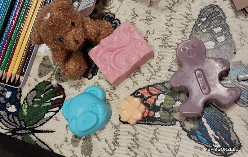 Na stole leżą kolorowe kredki, małe figurki misiów i mydełka w kształcie misia oraz innych wzorów.