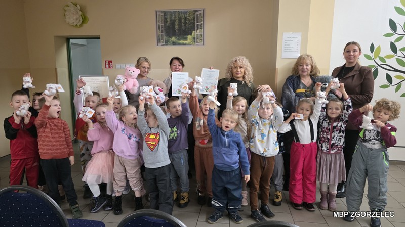 Wspólne zdjęcie uczestników spotkania – grupa dzieci i dorosłych stoi razem, trzymając pluszowe misie i podziękowania.