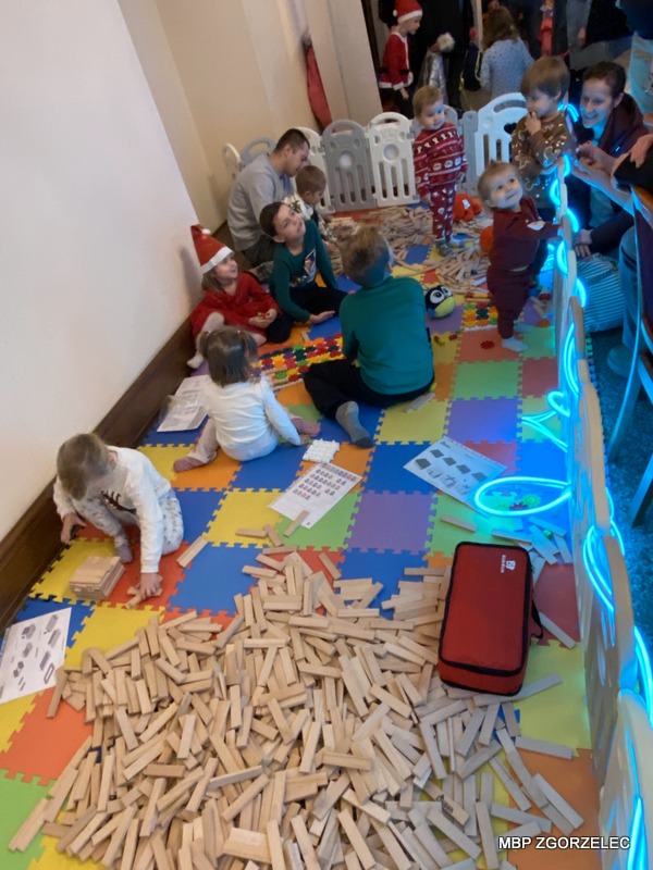 Grupa dzieci i dorosłych buduje różne konstrukcje z drewnianych klocków. Grupa dzieci i dorosłych buduje różne konstrukcje z drewnianych klocków.