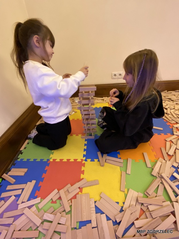 Dwie dziewczynki budują wieżę z klocków na kolorowej macie Dwie dziewczynki budują wieżę z klocków na kolorowej macie