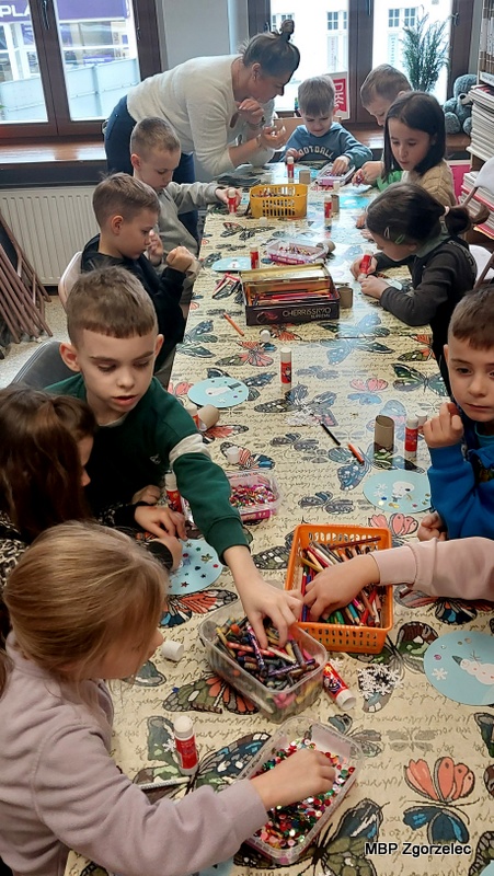 Dzieci tworzą zimowe prace plastyczne przy wspólnym stole w&nbsp;bibliotece.