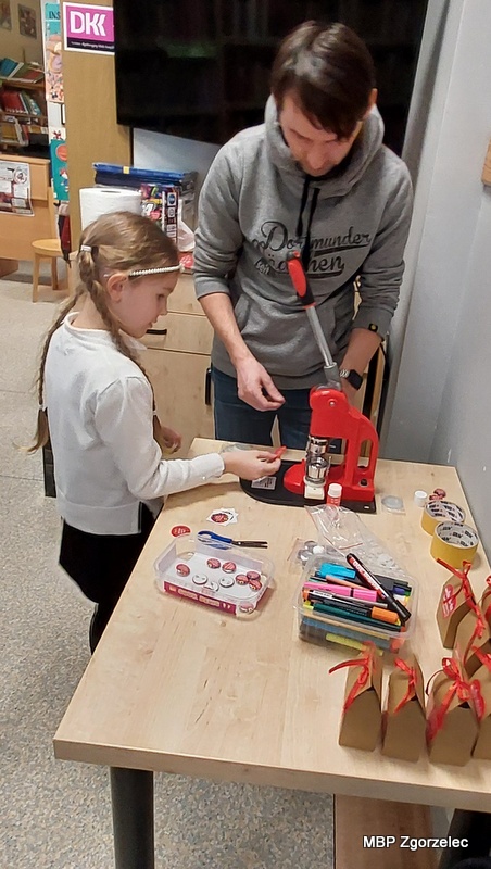 Dziecko wykonuje przypinkę WOŚP przy użyciu prasy do badge’y, podczas warsztatów przygotowanych przez Miejską Bibliotekę Publiczną.