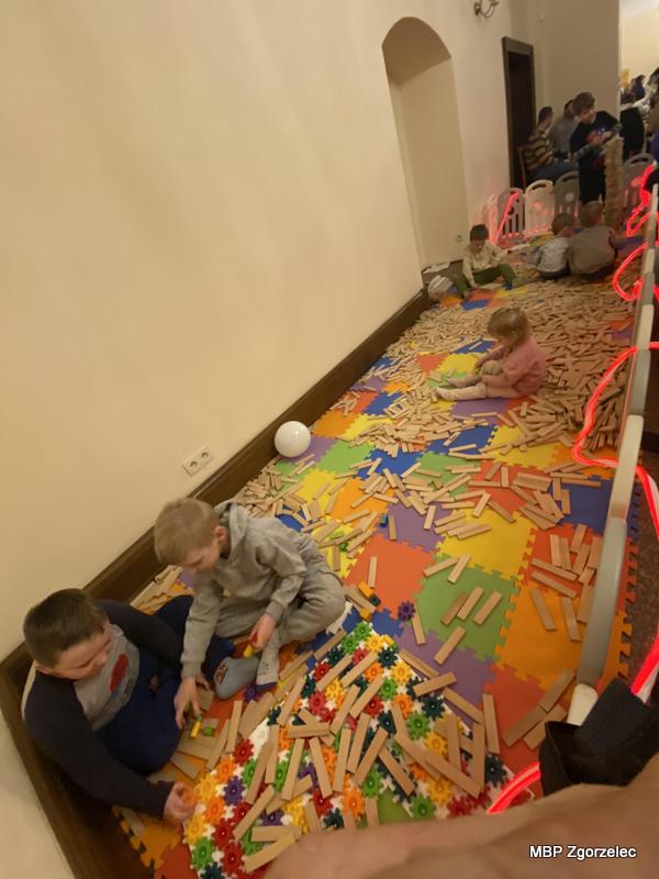 Dzieci bawią się drewnianymi klockami i&nbsp;konstrukcyjnymi elementami na dużej kolorowej macie, budując swoje projekty podczas atrakcji przygotowanych na finał WOŚP.