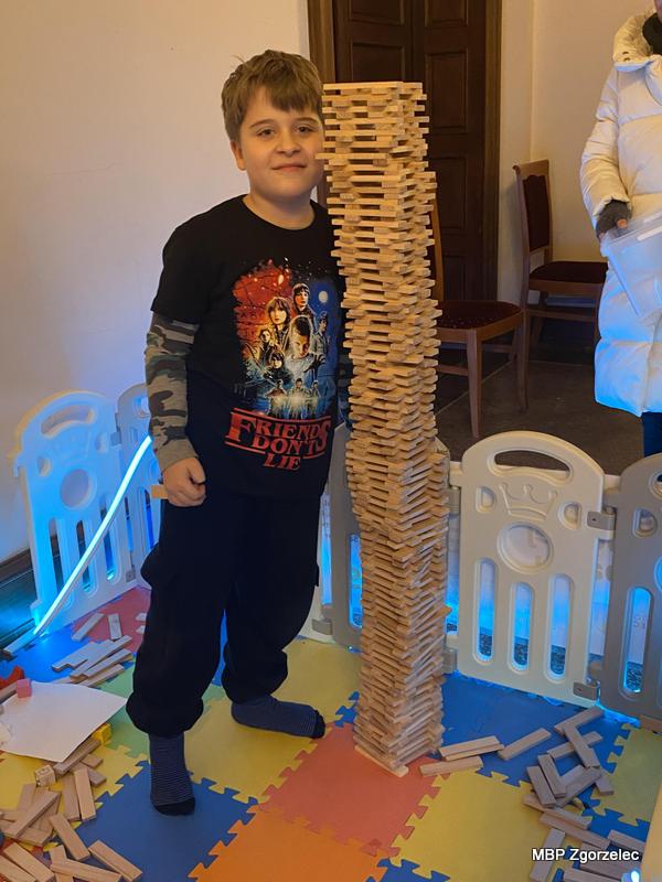 Chłopiec prezentuje imponująco wysoką wieżę z&nbsp;drewnianych klocków zbudowaną na kolorowej macie w&nbsp;strefie zabaw podczas wydarzeń WOŚP.