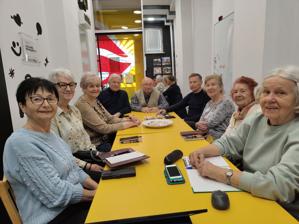 Uczestnicy zajęć edukacji cyfrowej dla seniorów siedzą przy stole w&nbsp;Filii nr 1 przy ul. Orzeszkowej 30a.