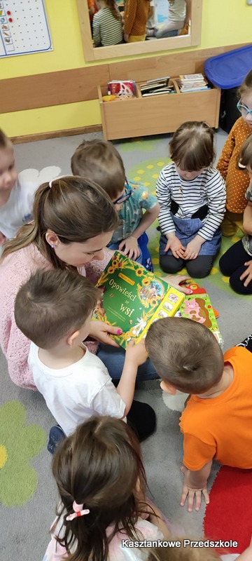 Dzieci zgromadzone na dywanie oglądają książkę dźwiękową o&nbsp;tematyce wiejskiej, poznając zwierzęta i&nbsp;urządzenia spotykane na wsi.