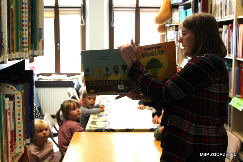Podczas głośnego czytania dzieci słuchają fragmentów książki „Podróż Pana Brokuła” prezentowanej w Oddziale dla Dzieci i Młodzieży.
