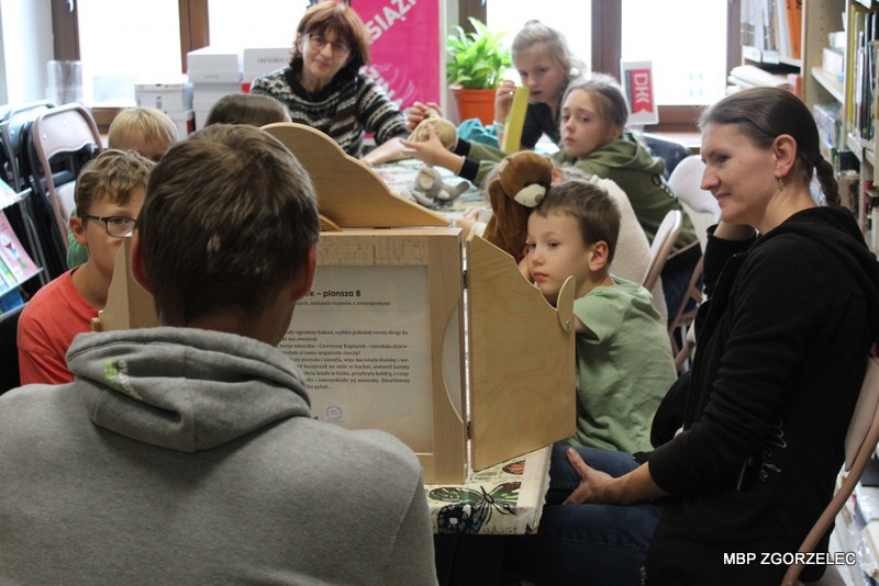 Dzieci uczestniczą w warsztatach plastycznych i przygotowują kartonowe teatrzyki inspirowane baśnią „Czerwony Kapturek”. Na stole znajdują się pudełka, kolorowy papier, nożyczki i materiały plastyczne. Dzieci uczestniczą w warsztatach plastycznych i przygotowują kartonowe teatrzyki inspirowane baśnią „Czerwony Kapturek”. Na stole znajdują się pudełka, kolorowy papier, nożyczki i materiały plastyczne.